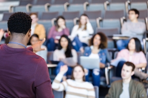 A male professor calls on a student in a lecture hall.