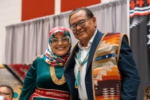 Navajo Technical University president Elmer Guy and Wafa Hozien, university academic administrator, stand together smiling at a campus event celebrating the new Ph.D. program. Both are wearing colorful Native prints.
