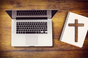 An image of a laptop next to a notebook with a cross lying on top of it.