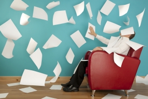 A man sits in an armchair as blank white pieces of paper float around him.