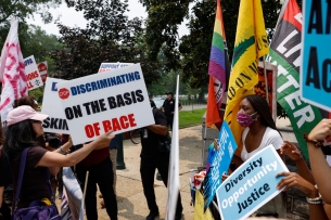 Dueling groups of demonstrators face off holding signs that say "stop discriminating on the basis of race" and "we are the people."