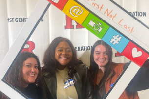 Three first-generation students smile at a Rutgers University first-gen event with a photo-booth frame