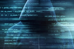 A hooded figure with a hidden face stands in front of a background of digital code