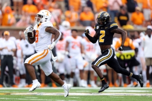 Two football players running, one in front with a ball.