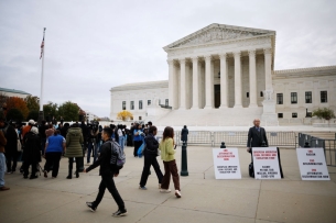 The scene in front of the Supreme Court Oct. 31, when the court heard arguments in two cases challenging race-conscious admissions in higher education: a lone opponent of affirmative action, with protest signs, stands next to a group of mostly young people rallying in support of affirmative action.