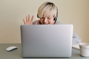 A student waves to their laptop webcam on a video call.