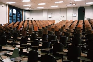 An empty lecture hall full of brown chairs.