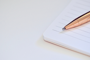 An orange pen rests on a blank sheet of white lined paper.