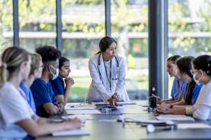 A group of nursing students sits around a long conference table looking at the instructor