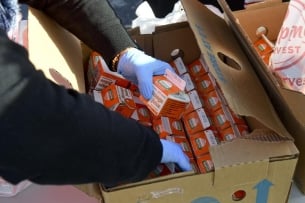 A photo of gloved hands sorting through a box of orange juice cartons.