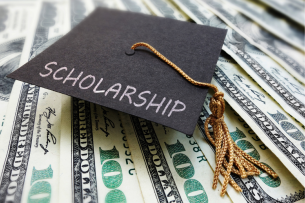 A graduation cap with the word "SCHOLARSHIP" written on it atop a spread of $100 bills.