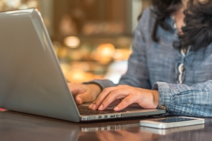 Close-up photo of a woman's hands typing on a laptop keyboard.