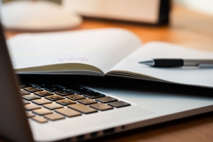 Laptop Computer on a Modern Wooden Business Desk with a Notepad and Pen in Unfocused Background