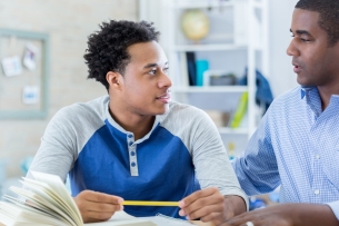 Black male student listens attentively to older adult giving guidance.