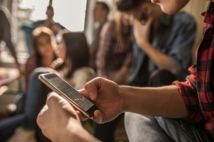 Unrecognizable male student text messaging on mobile phone while on a break in the classroom.