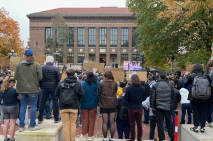 The backs of students holding signs outside of a large building.