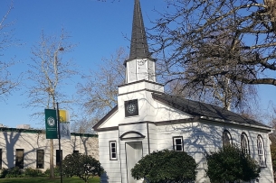 An exterior view of the Multnomah University campus showing trees, blue sky and a white building with a steeple.