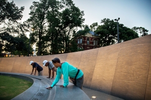 Three Black people touch the names on a slave memorial.