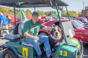 President Chuck Seifert sits in a green golf cart with school mascot, Baloo.