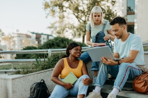 Three college students of different ethnicities are sitting outside and working on a group project together.