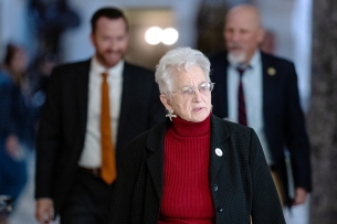 Virginia Foxx walks in a hallway, wearing a red shirt and black blazer