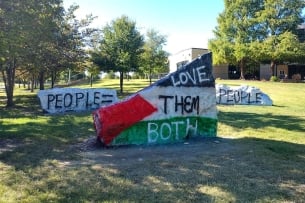 A photo of three rocks, two of which read "people = people," one of which says "love them both" over the Palestinian flag.