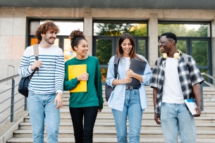 Four smiling students walk together in front of a campus building. 