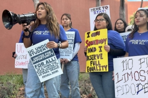 A group of undocumented students hold protest signs. One yells into a bullhorn.