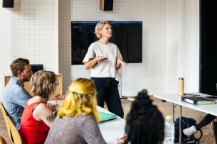 A female professor addresses a group of students in a small seminar.