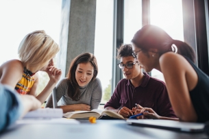 Four students work at a table looking at open books.