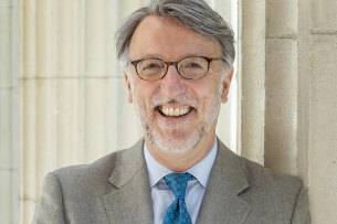 A man in glasses and a suit with blue tie smiling