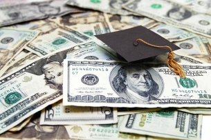 a grad cap sits on a pile of dollar bills