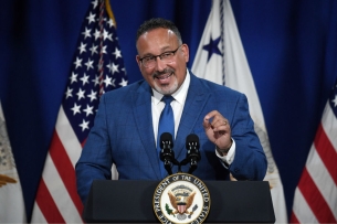 A man in a blue suit and tie at a podium in front of American flags