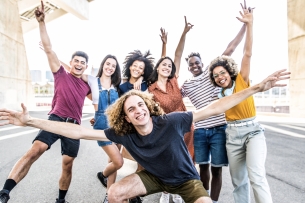 A big group of happy friends stands together with raised arms.