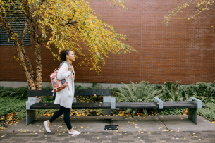 A woman carrying a backpack walks outside on a college campus