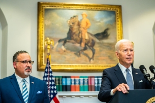 Miguel Cardona stands next to President Joe Biden in the Roosevelt Room of the White House.