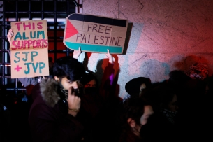 Protesters lit by a red and white light hold signs reading: "This alum supports SJP and JVP" and "Free Palestine"