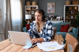 Happy woman wearing wireless headphones working on laptop at home office