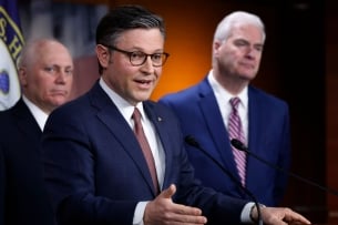 Three white men in suits stand at a podium