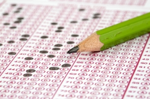 A green number 2 pencil lies atop a multiple choice answer sheet with some bubbles filled in.