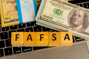 Wooden blocks spell out “FAFSA” atop a computer keyboard, next to two stacks of cash money.