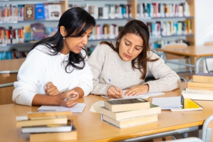 Two females students sit at a desk writing together