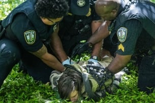 A person held face-down in the grass by several police officers.