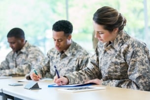 Military students working at a table using pen and paper.