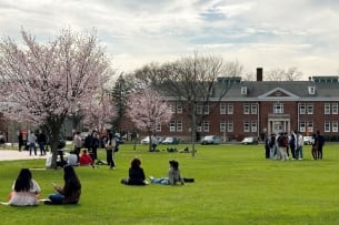 Students sit on a lawn outside academic buildings at Nassau Community College.