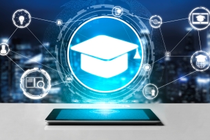 A tablet rests on a table and has a glowing, digitized graduation mortar cap above it