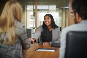 A young woman in a gray blazer shakes hands with an interviewer