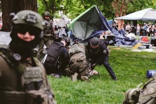 Police surrounding a protester during arrest with tents in the background