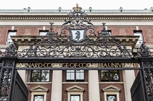 The front gate of Barnard College. A brick building is in the background with a wrought iron fence in the front, which says "Barnard College of Columbia University" 