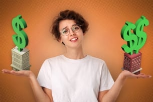 A person in a T-shirt and glasses holds two mini buildings with dollar signs over them